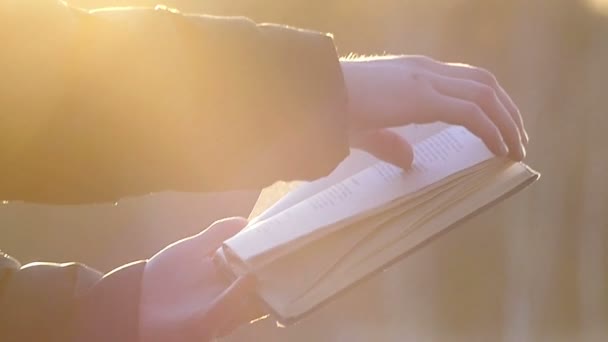 Krásně osvětlené rukou otočit stránky knihy při západu slunce na rozostřeného pozadí ve zpomaleném záběru - Záběry, video