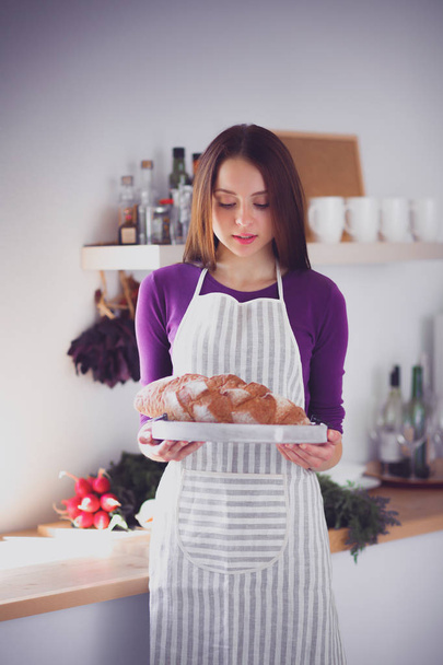 Young woman holding tasty fresh bread in her kitchen - Foto, afbeelding