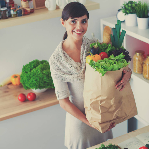 Young woman holding grocery shopping bag with vegetables Standing in the kitchen - Foto, Imagen