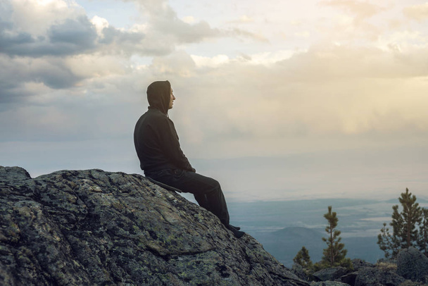Ο άνθρωπος κάθεται σε έναν πέτρινο λόφο, τα χέρια να βλέπουν την προβολή από τα ύψη και απολαμβάνει την ελευθερία - Φωτογραφία, εικόνα