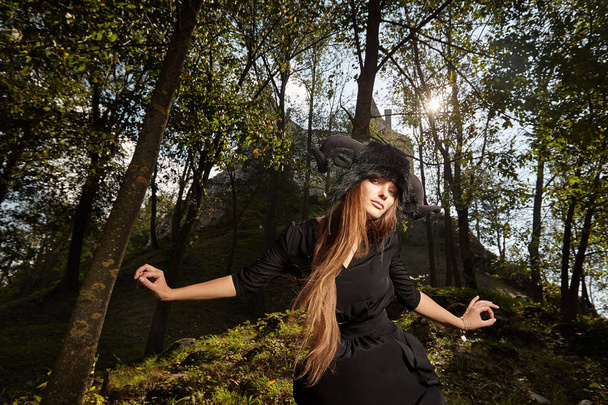 Modelo chica en un vestido negro y sombrero negro caminando en un místico
  - Foto, Imagen