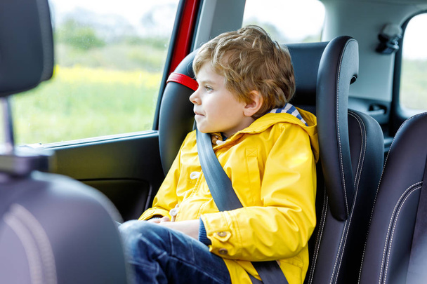 Adorável menino pré-escolar bonito sentado no carro em casaco de chuva amarelo
. - Foto, Imagem