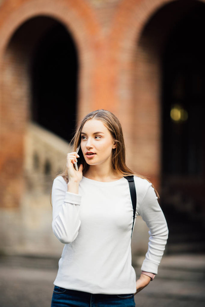 Happy student girl walking and calling on mobile phone outdoors with a Uni background - Fotoğraf, Görsel