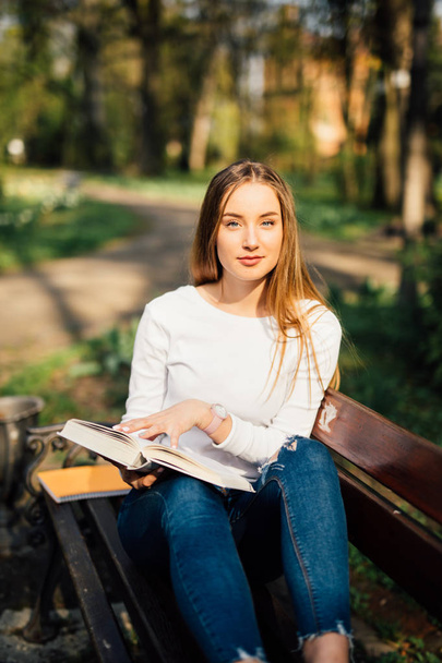 college student girl reading a book sitting on bench in city park - Foto, Imagen