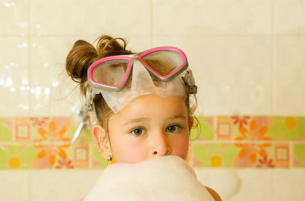 little beautiful girl playing with water and foam in bath using a swimsuit and beautiful dive sunglasses - Foto, imagen