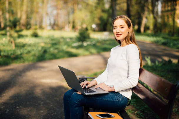 Chica joven en un banco con un ordenador portátil en el parque
 - Foto, imagen