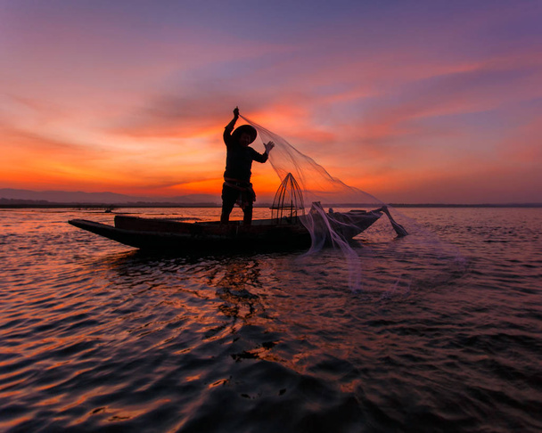 Silhouette of Asian fisherman on wooden boat throwing a net for