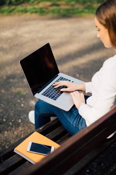 Femme assise sur le banc à l'extérieur et travaillant sur ordinateur dans le parc
 - Photo, image