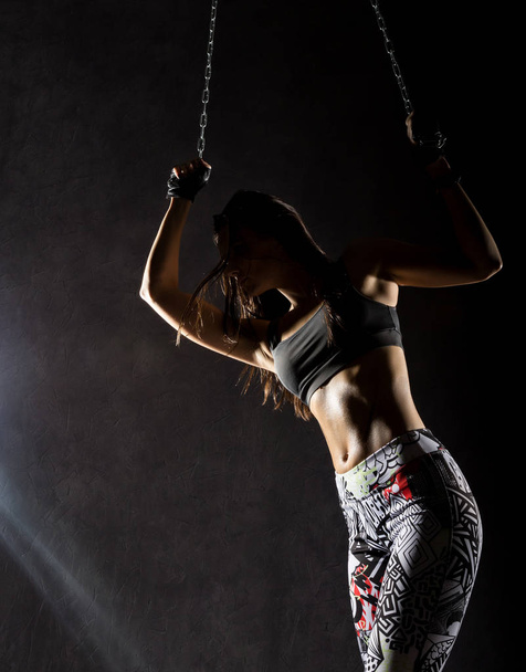 sexy strong muscular woman with iron chain on dark background in the beam of a searchlight - 写真・画像