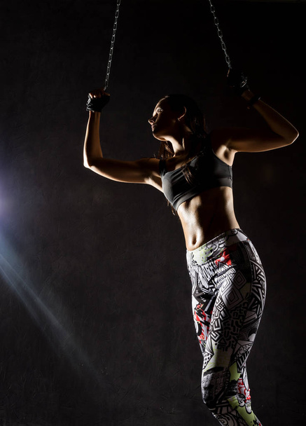 sexy strong muscular woman with iron chain on dark background in the beam of a searchlight - Fotografie, Obrázek