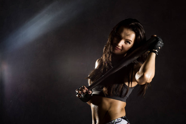sexy athletic woman with baseball bat on dark background in the beam of a searchlight - Фото, зображення