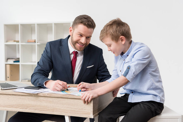 Бизнесмен рисует на деловых бумагах с сыном
 - Фото, изображение