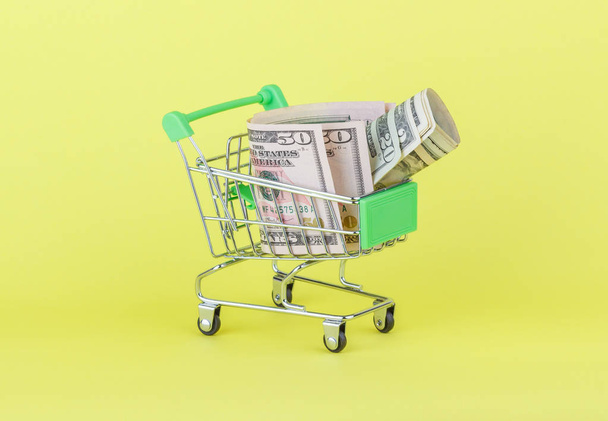 Amerikaanse dollars in de winkelstraat pushcart, gele achtergrond - Foto, afbeelding