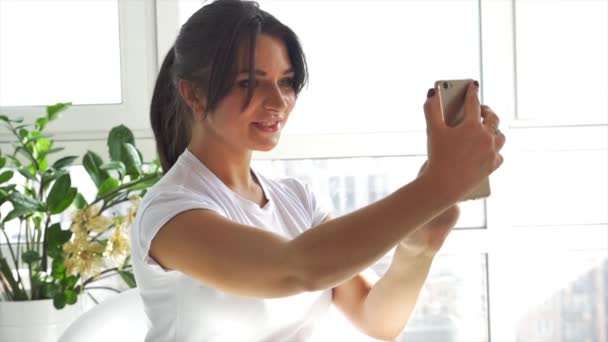 Caucasian girl in white t-shirt holding a smartphone - Filmati, video