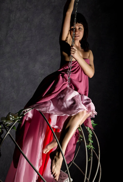 menina elegância sexy em uma saia rosa, balançando em um balanço de metal. agarrar-se às correntes
 - Foto, Imagem