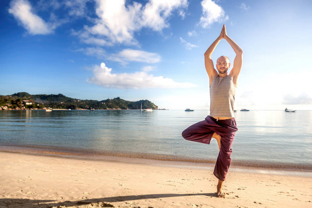 Young attractive man practices yoga on the beach at sunrise - Fotografie, Obrázek