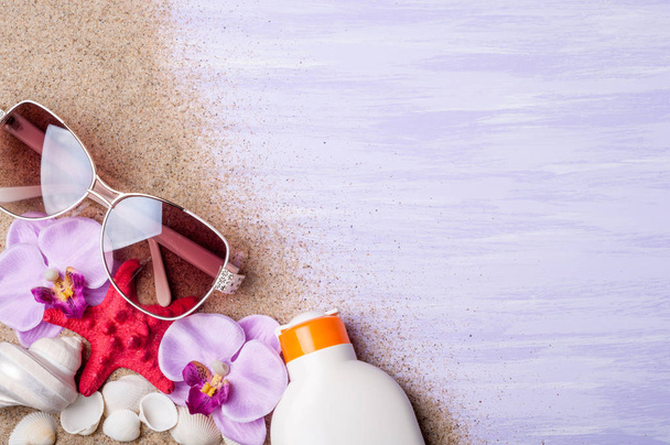 Summer holiday background. Beach accessories sunglasses, sunscreen and seashells on purple surface top view. Vacation and travel concept. - Photo, Image