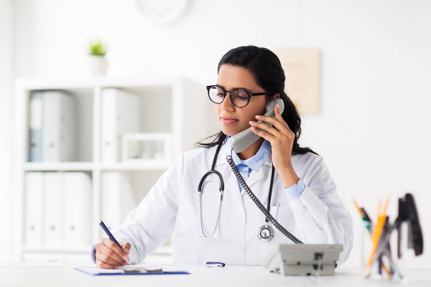 doctor with clipboard calling on phone at hospital - Valokuva, kuva