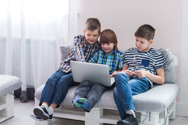 Children at home sitting on sofa, playing with laptop - Фото, изображение