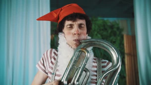 Joyful man in dwarf costume playing old tin tuba stick tounge out of breath - Footage, Video