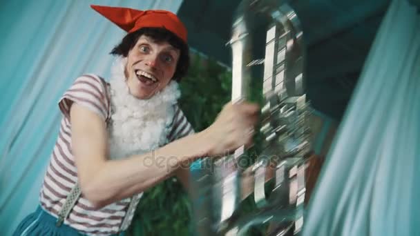 Joyful man in dwarf costume fooling around with weary broken tin tuba in hands - Footage, Video