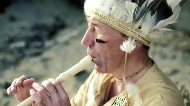 An Indian in a national costume plays a flute near a boat on the river bank 4k - Footage, Video