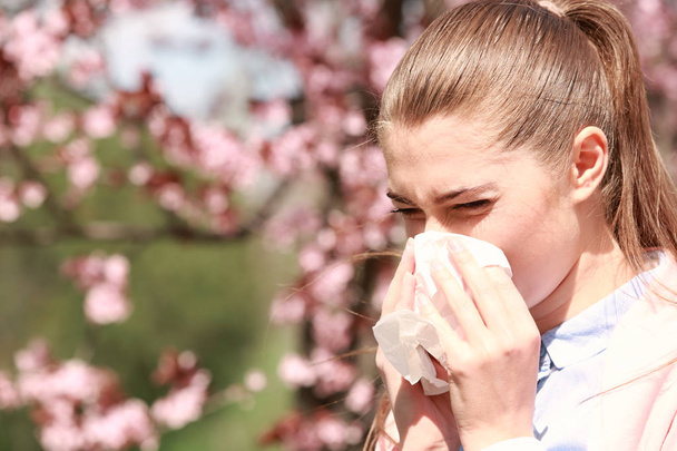 Sneezing young girl with nose wiper among blooming trees in park - Foto, Bild