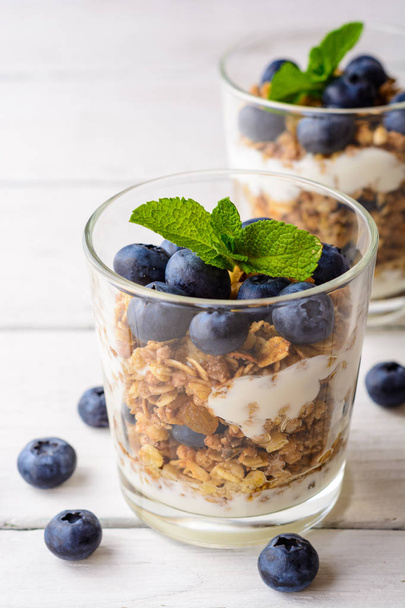 Granola with yogurt and blueberries in glass on white wooden table. - Zdjęcie, obraz