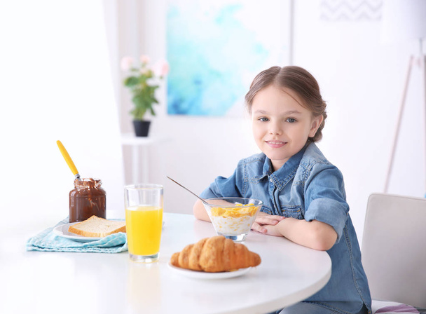 Cute little girl having breakfast at home - Foto, afbeelding