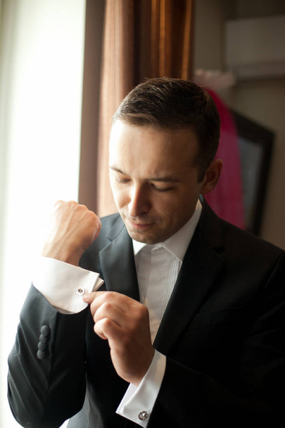 Groom adjusts the cufflinks standing in the light of morning sun - Photo, Image