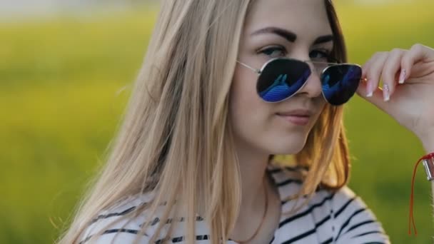 Meisje zittend op het gras in zonnebrillen en knipogen naar camera - Video