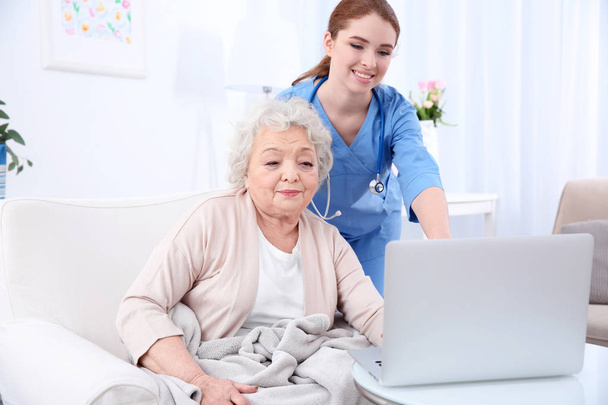 Nurse helping elderly woman to work on laptop in light room - Foto, Bild