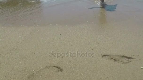 Női láb áthelyezése a homokos tengerparton lassítva a tenger hullámai - Felvétel, videó
