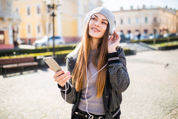 Mujer escuchando música en línea con auriculares inalámbricos desde un teléfono inteligente en la calle en un día soleado de verano
 - Foto, imagen