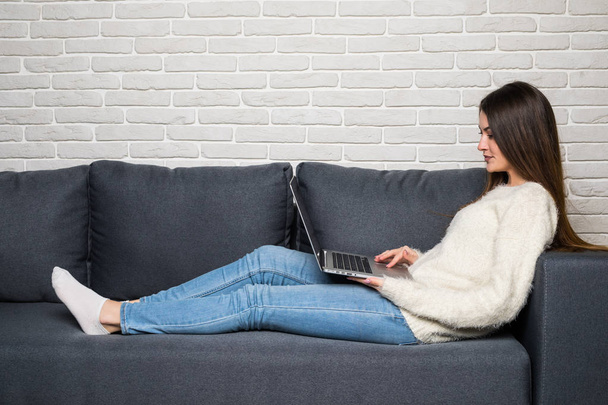 Onnellinen nainen istuu sohvalla käyttäen hänen kannettava kotona olohuoneessa
 - Valokuva, kuva