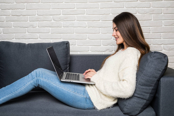 Femme heureuse assise sur le canapé en utilisant son ordinateur portable à la maison dans le salon
 - Photo, image