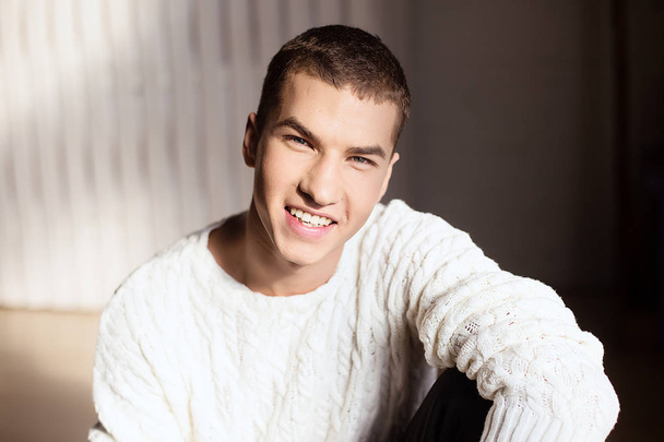 Προσωπογραφία άνδρα στο λευκό πουλόβερ στο studio με φως ημέρας - Φωτογραφία, εικόνα