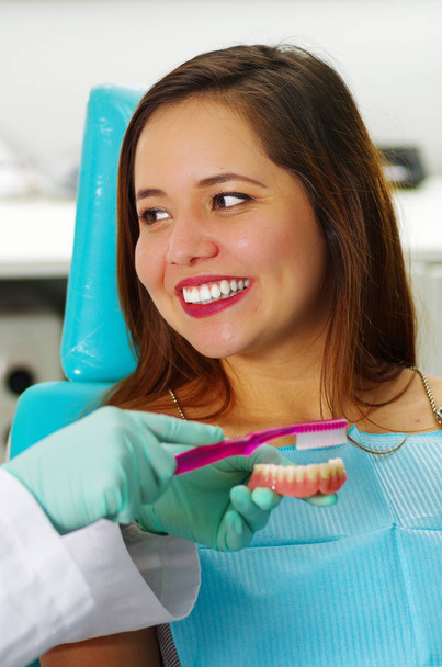 Krásná žena pacient s úsměvem, zatímco doktor je kartáčování falešný zubní plak v kanceláři lékaři - Fotografie, Obrázek