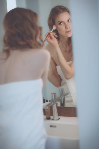 Young woman looking in the mirror and putting make-up on - Foto, Imagen