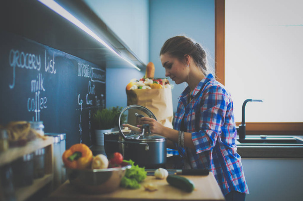 Young woman standing by the stove in the kitchen - Foto, Bild