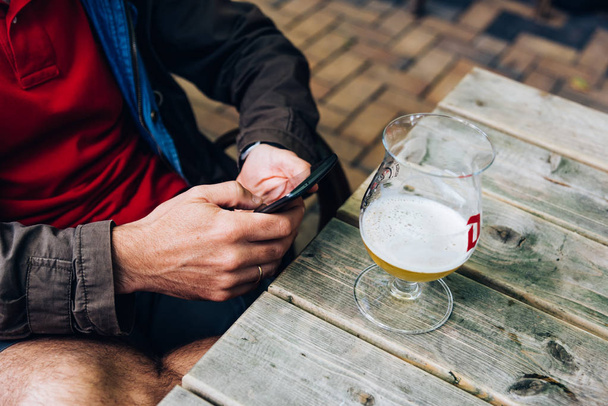 Mies tekstailee puhelimessa juodessaan olutta baarissa.
  - Valokuva, kuva