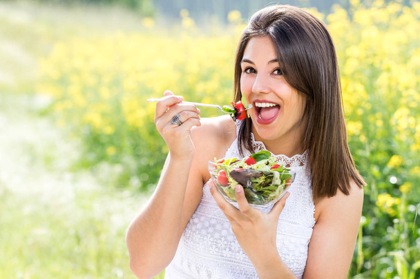Attractive healthy girl eating green salad outdoors. - Photo, Image