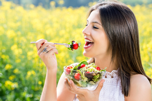 Healthy girl eating salad outdoors with flower field in backgrou - Photo, Image