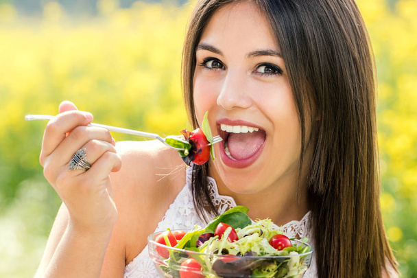 Fun portrait of cute girl eating green salad outdoors. - Photo, Image