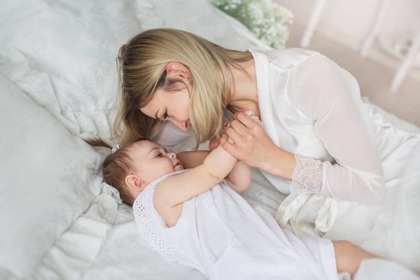 Happy young mother plays with her little baby on a bed - Foto, Imagem
