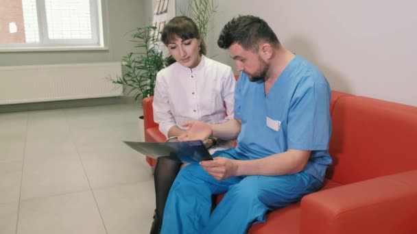 Dwóch lekarzy, mężczyzna i kobieta są siedzi na kanapie w klinice i rozmawiają ze sobą. 4k - Materiał filmowy, wideo