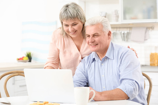 Midden ouder echtpaar met laptop op keuken - Foto, afbeelding