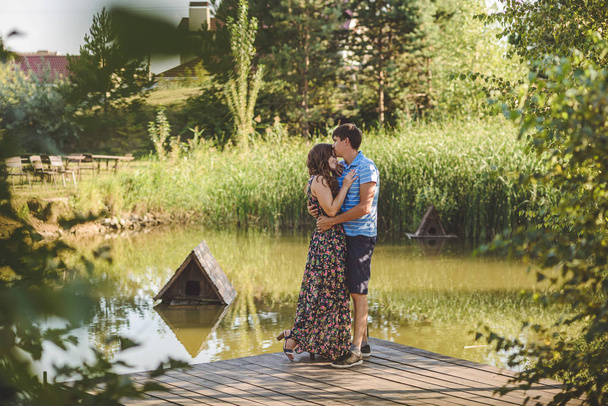 Happy romantic couple on a wooden bridge near the lake. Man embraces a young woman. - Photo, Image