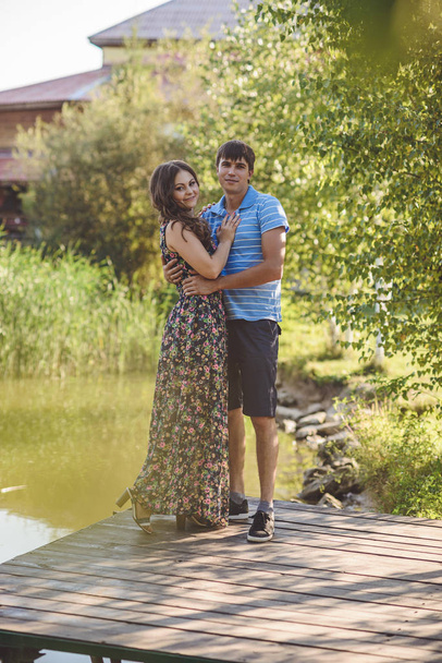 Happy romantic couple on a wooden bridge near the lake. Man and young woman looking at the camera. - 写真・画像
