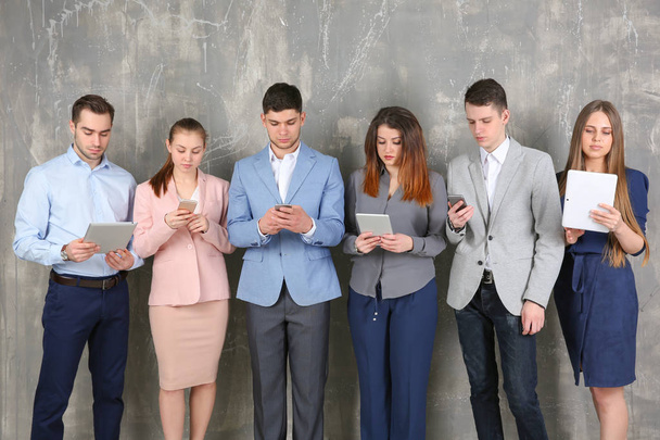 Young people in business clothes using digital devices on gray textured background - Zdjęcie, obraz
